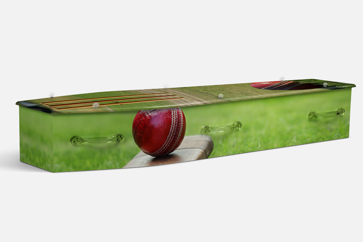 Cricket coffin showing a red cricket ball resting on a bat beside the stumps on green grass
