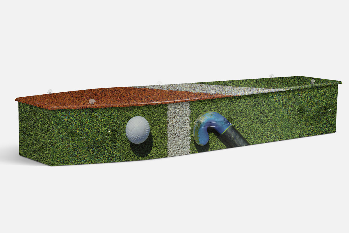 Field Hockey coffin with a hockey ball and stick on green turf beside a red running track