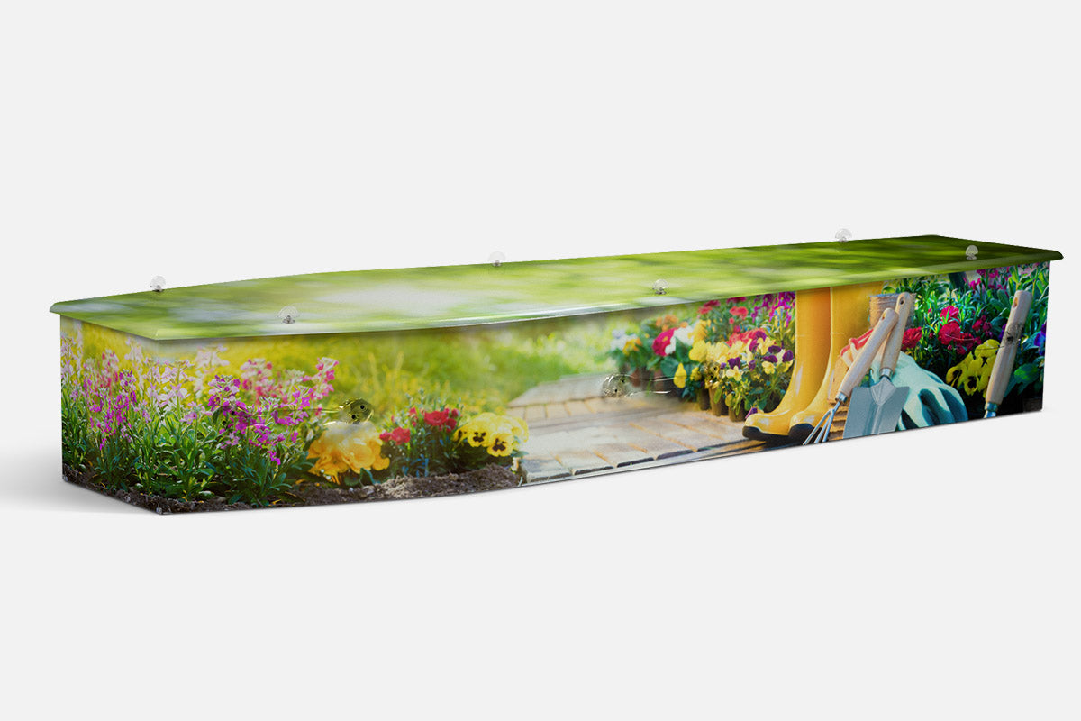 Gardening coffin in a photographic garden scene with flowers, a path, yellow gumboots and tools