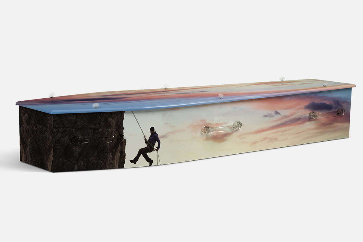 Rock Climbing coffin with a silhouetted climber on a cliff face against a pink sunset sky